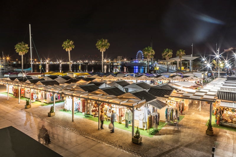 Night view of Malaga touristic port with little shops market and the sea in the background.