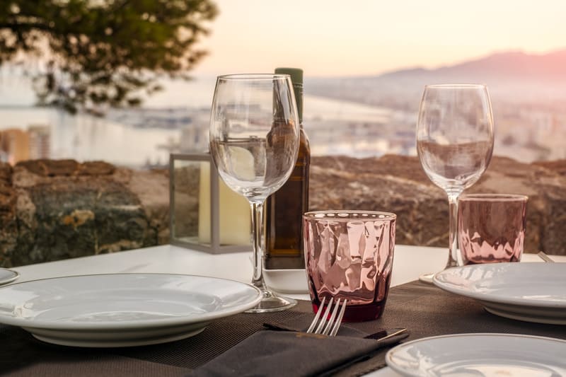 close up of a table with a wine glasses, wine, and plates overlooking a city and a tree background