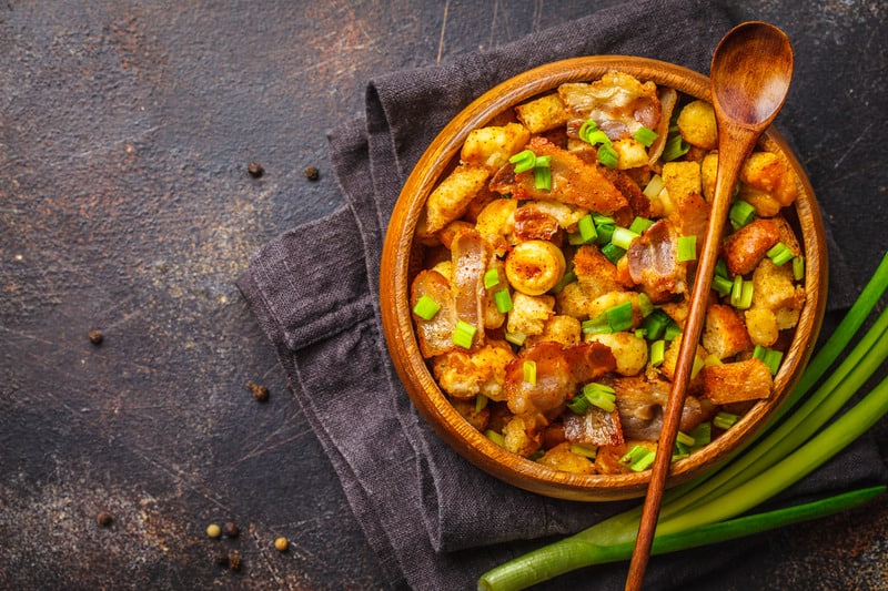 Spanish migas with pork and green onions in wooden bowl on a dark background.