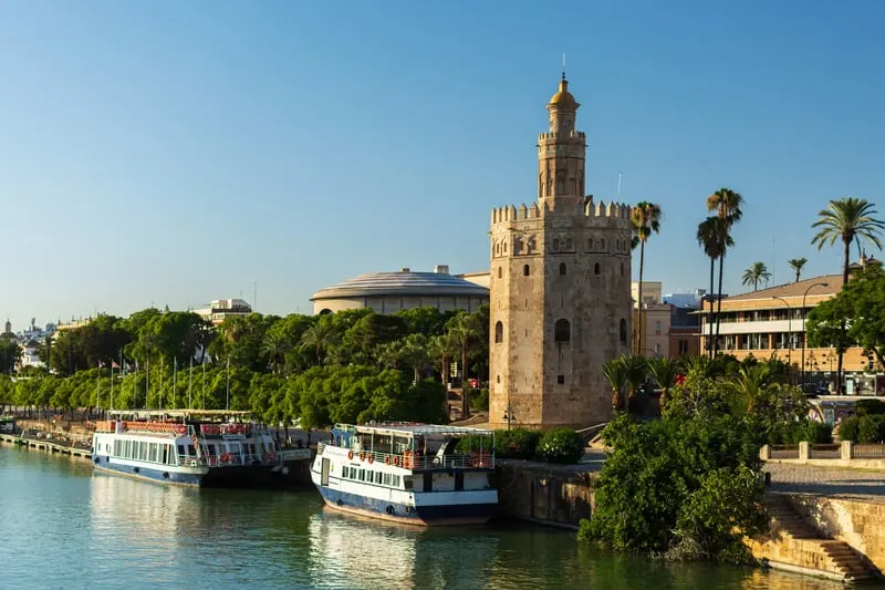 Torre de Oro by the river with two boats and palm trees