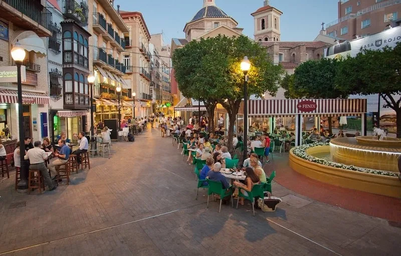 a view of plaza flores filled with people dining on tables and bars, almost at night time