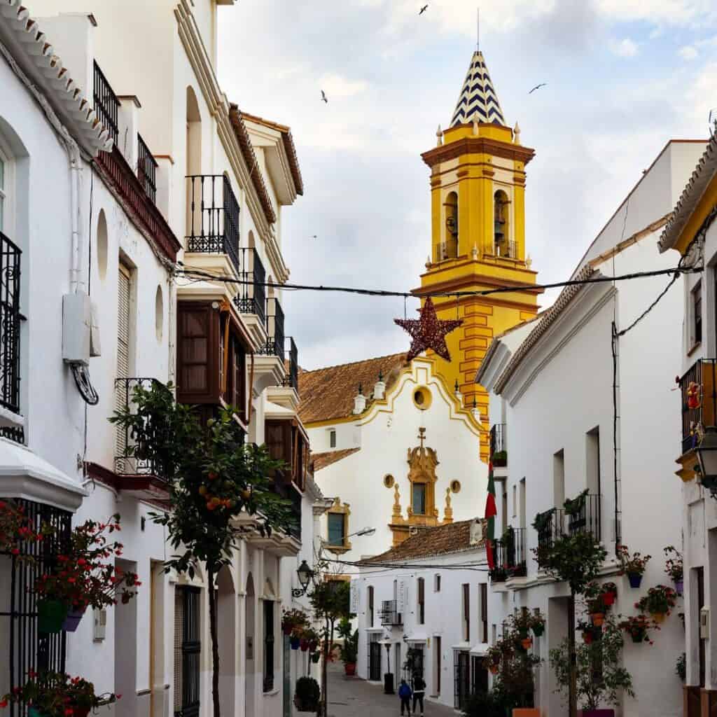 a narrow street with white buildings and a yellow tower