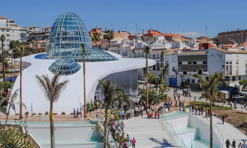 the Orchid House - a white building with a glass dome with people coming inside; and white houses on the background