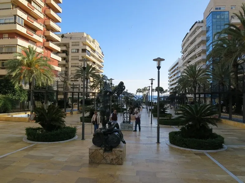 a tiled park with plants and lamp posts between big buildings