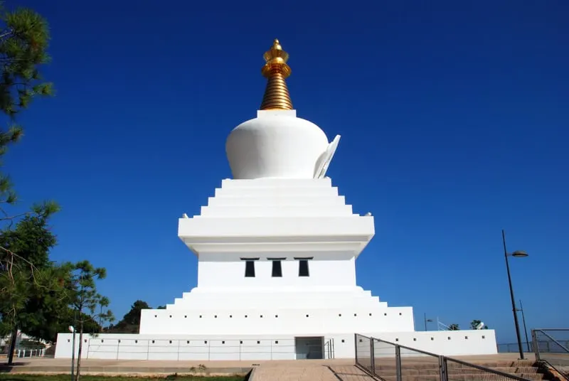 a white stupa with gold top under a blue sky