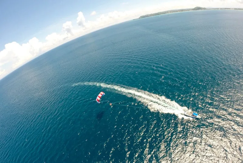 a curved aerial view of a person parasailing with blue waters and clouds on the side