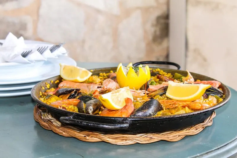 delicious paella in Granada restaurant, photo taken sideways with paella on a black plate with lemon and clams on the top