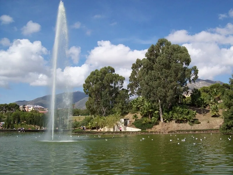 a lake in the Parque de la Paloma with a fountain on the middle and ducks floating, land filled with trees