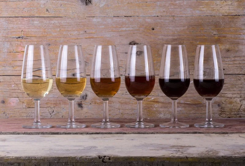 a line of Selection of Jerez Sherry wines with different colors on wine glasses with a wood background