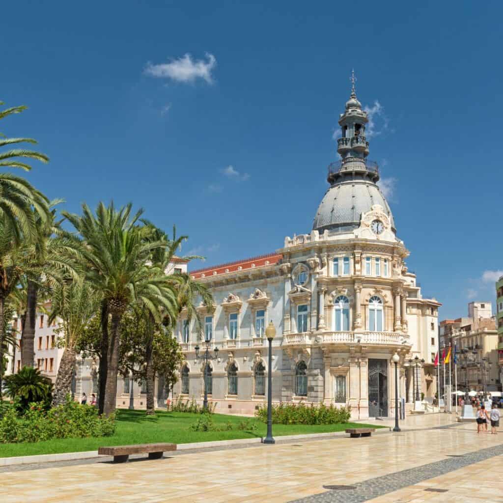 palm trees in front of a building with a tower on a plaza