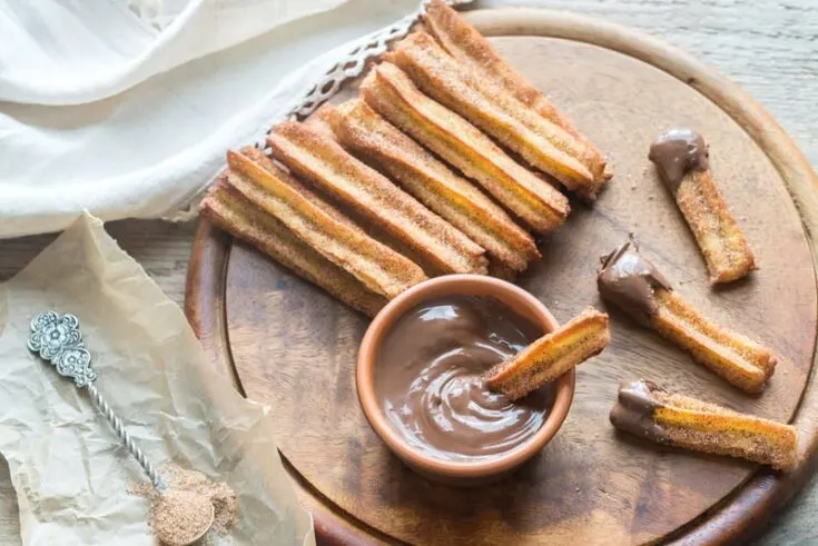 Homemade Churros served with chocolate sauce on a wooden board