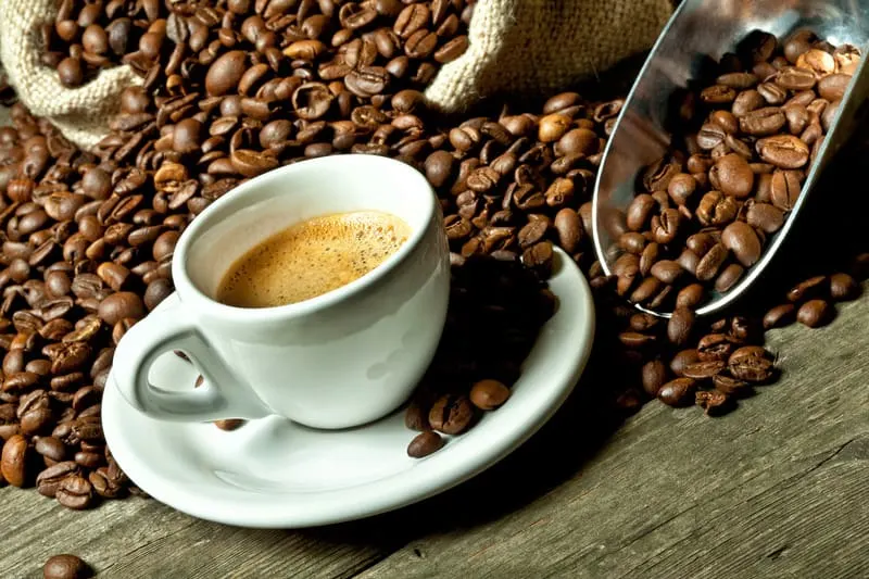 a closeup of a cup of coffee surrounded by real espresso and coffee grains