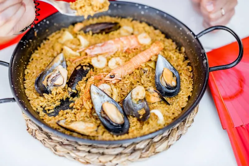 Pan with sea Paella, a Valencian rice dish, on the white table outdoors. 25 Ideas for the Best Spanish Themed Party 