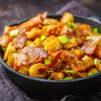 Spanish migas with pork and green onions in a cast-iron pan on a dark background.