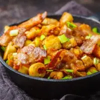 Spanish migas with pork and green onions in cast-iron pan on dark background.