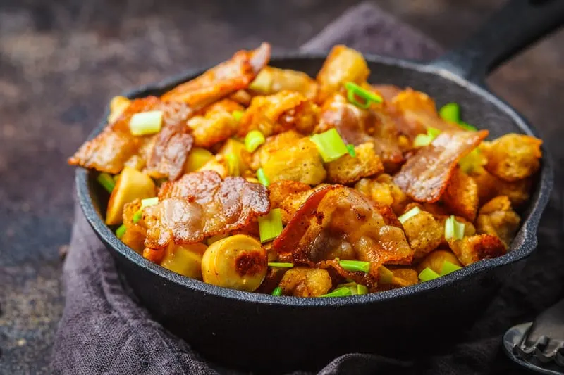 Spanish migas with pork and green onions in cast-iron pan on dark background.