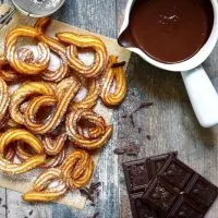 Traditional spanish breakfast dessert, churros with chocolate sause on a rustic background.