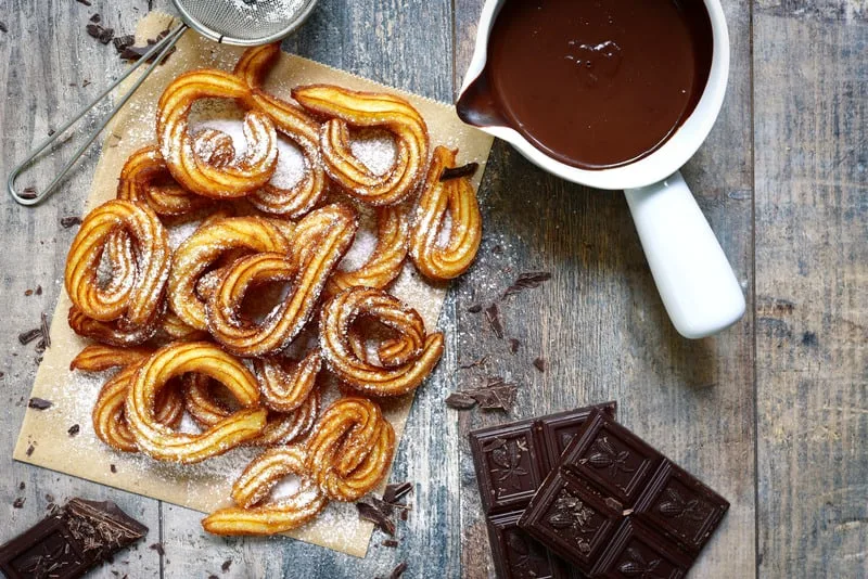 Traditional spanish breakfast dessert, churros with chocolate sause on a rustic background.