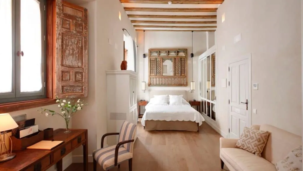 hotel corral del rey sevilla, a hotel room with a white and brown theme with a white bed, sofa, chair and table