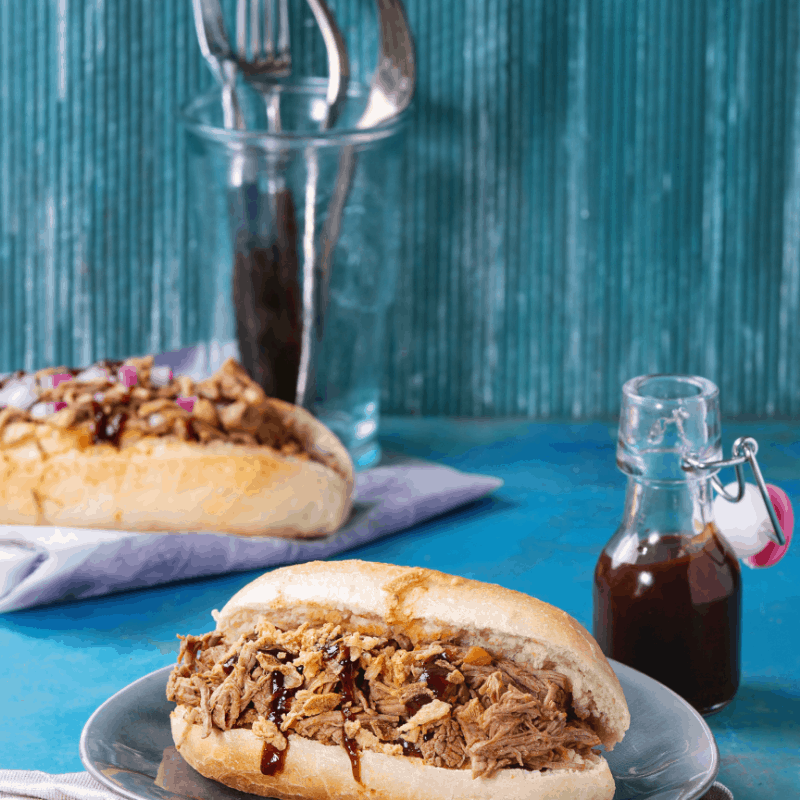 two pieces dried up meat inside sandwich on a plate with a bloody red sauce on the bottle