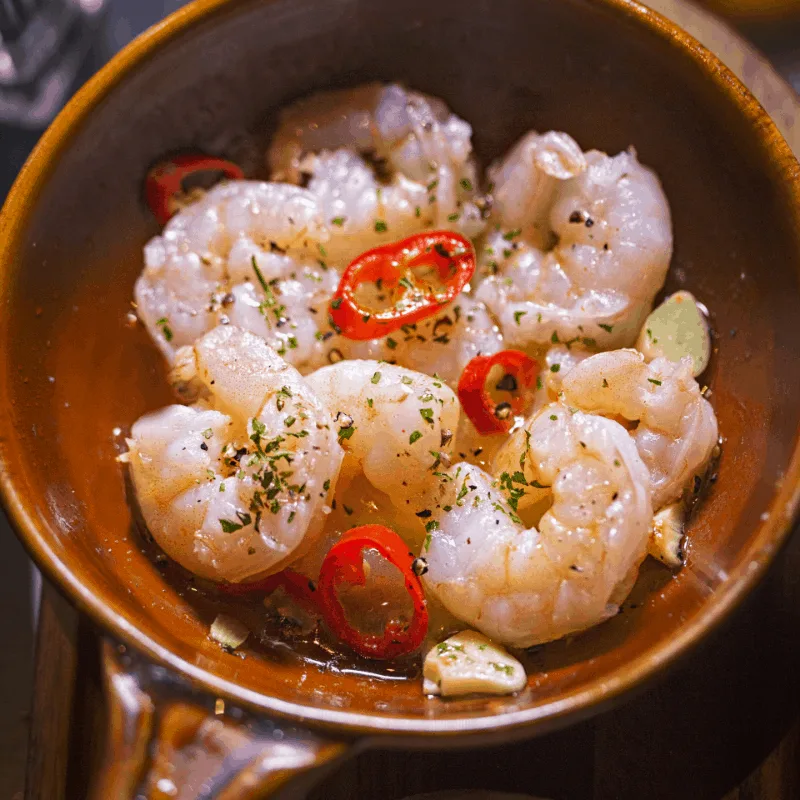 gambas al pil pil served in a clay pot, decorated with chilly  slices.