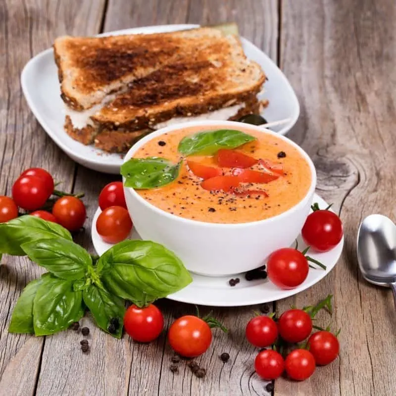 spicy Gazpacho served in a white bowl with toast next to it and cherry tomatoes. 