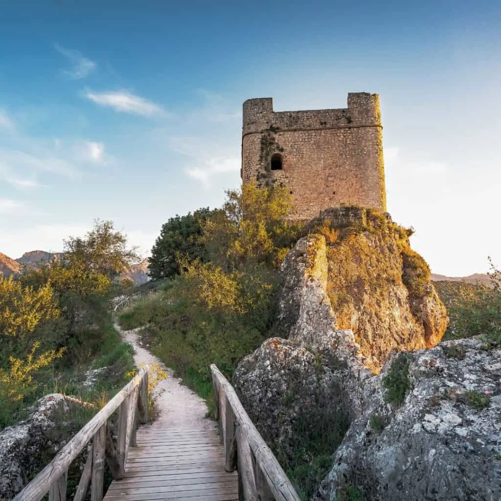 a wooden walkway to a footpath leading to Zahara de la Sierra Castle tower under the blue sky
