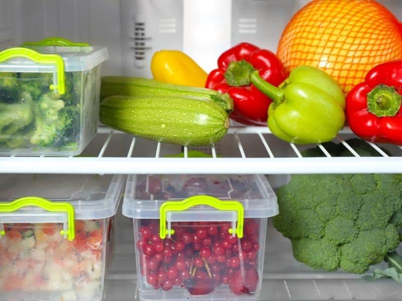 How to Store Bloody Mary Gazpacho. An open fridge with various vegetables and fruits in plastic containers.