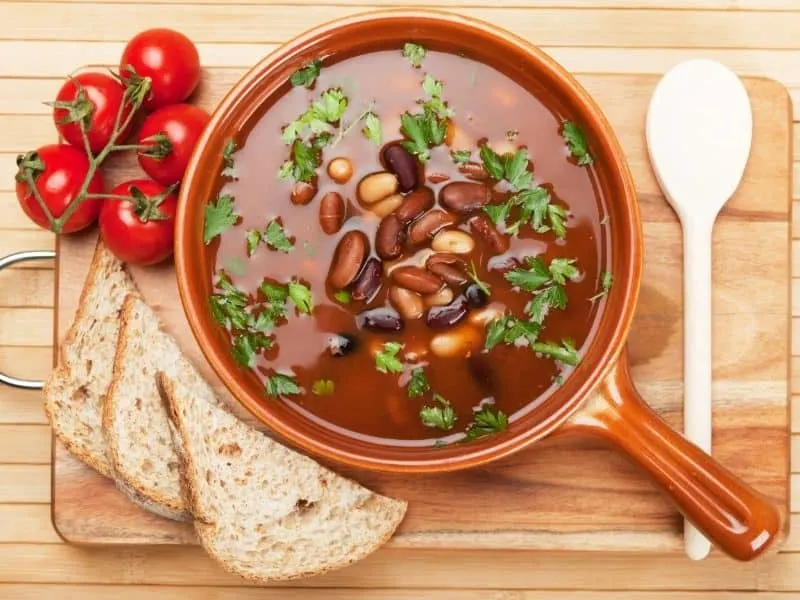 spanish vegan bean soup in a clay bowl next to bread and tomatoes