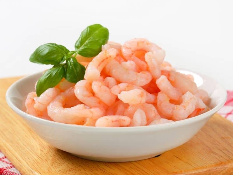 peeled shrimps in a white bowl on a wooden table for the shrimp croquettes recipe.