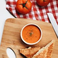 best tomato gazpacho served with grilled cheese sandwich on a wooden board.