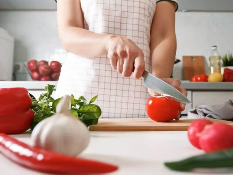 Woman cuts tomato on cutting board for the spanish chickpea salad.