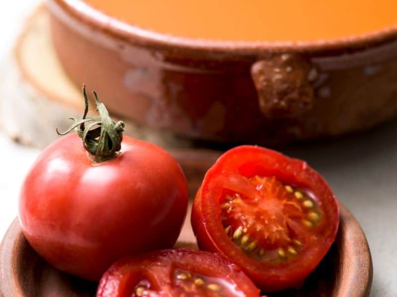 ripe tomatoes next to a clay bowl of heirloom tomato gazpacho