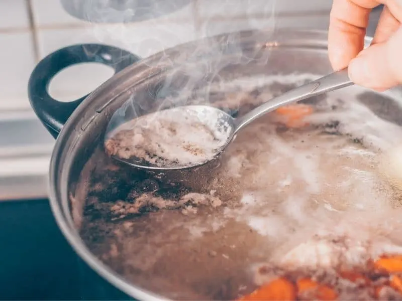 Cook with a spoon removes the foam from the boiling mackerel soup recipe