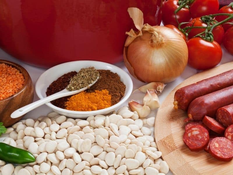 ingredients for spanish chorizo soup such as beans, onions, tomatoes and spices on a wooden table. 