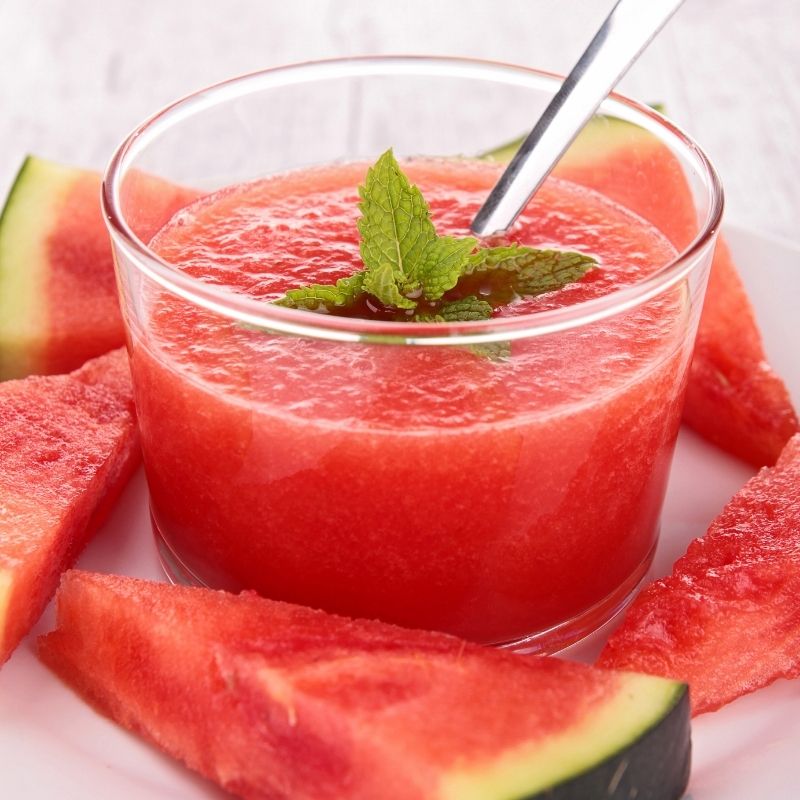 Watermelon tomato Gazpacho in a glass bowl with chunks of watermelon next to it. 