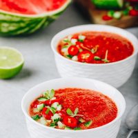 Gazpacho tomato gazpacho in 2 bowls with a watermelon in the background.