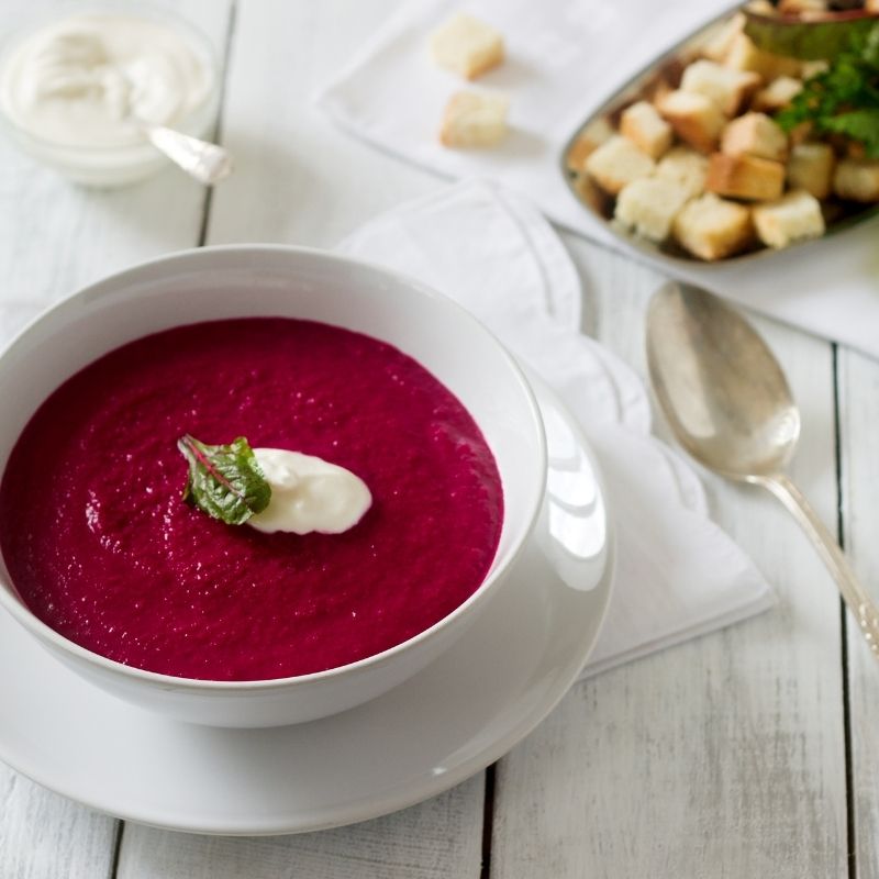 blueberry cold soup in a white bowl with bread croutons next to it.