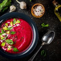 beetroot gazpacho served in a black bowl decorated with fresh vegetables.