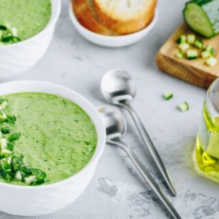 Spanish cucumber soup recipe in bowls served with toast and spoons on a table