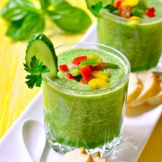two glasses of Spanish cucumber soup recipe in a glass with toppings of slices of red, yellow, and green varnished with a cucumber and bread on a serving plate. cucumber gazpacho recipes