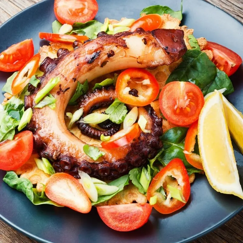Spanish grilled octopus salad recipe with tomatoes on a blue plate.