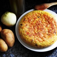 vegan spanish omelette on a white plate with onion and potato next to it.
