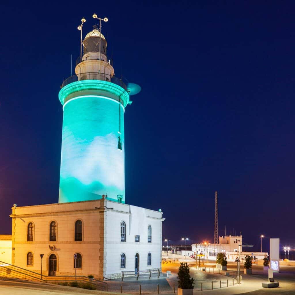 a lighthouse during the night with blue lights and buildings at the back