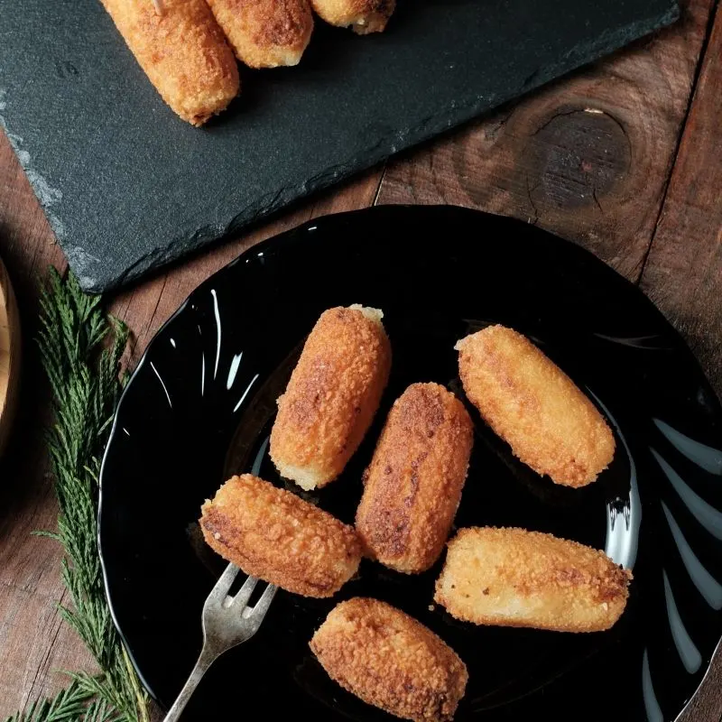 chicken croquette on a black plate with a fork on a wooden table