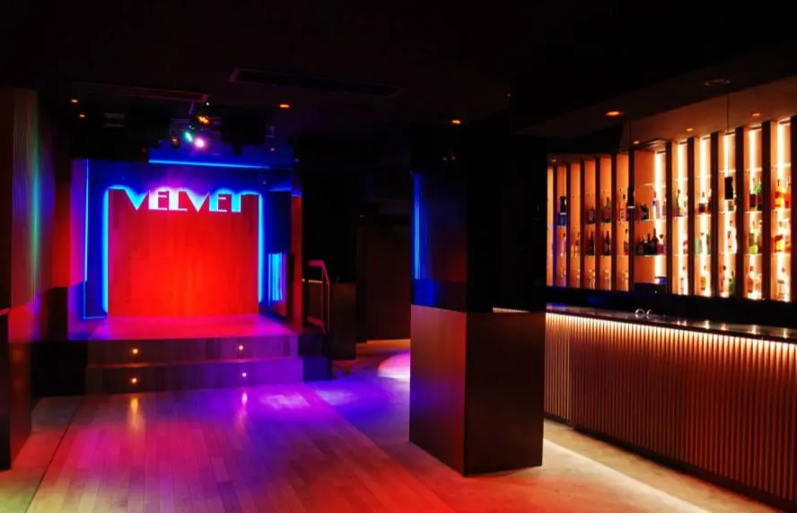 an interior of Velvet Club with a dark pathway and stage with red and blue lights