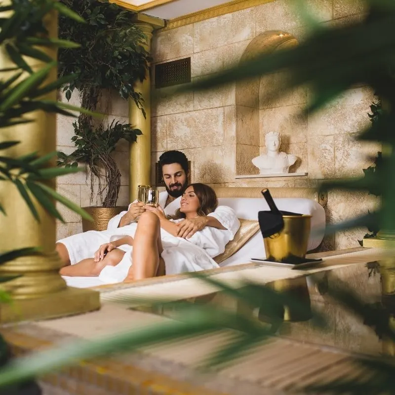 a couple laying together at a pool chair while drinking wine and a view of leaves