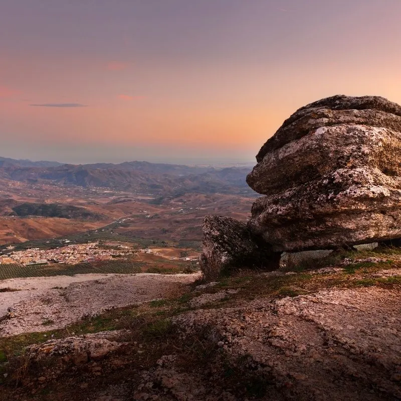 view of the El Torcal Antequera, unique rock formation atop a mountain overlooking a small town during sunset time