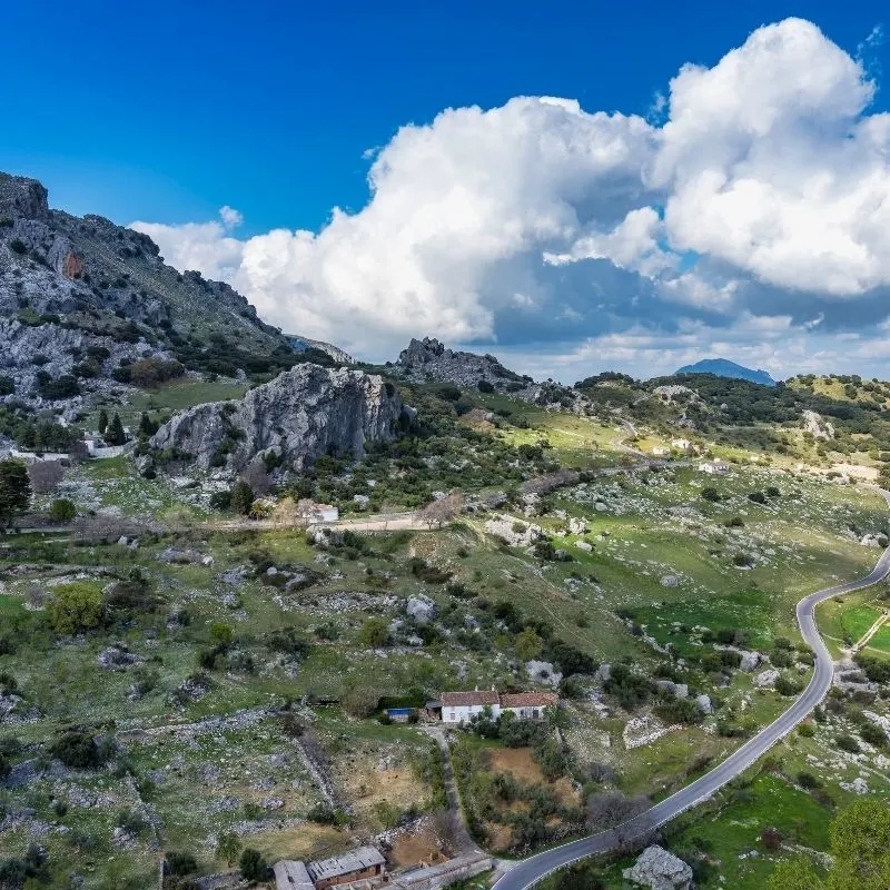 big clouds, a granite looking mountain or cliff - SIERRA DE GRAZALEMA NATURAL PARK with houses and trees at the bottom