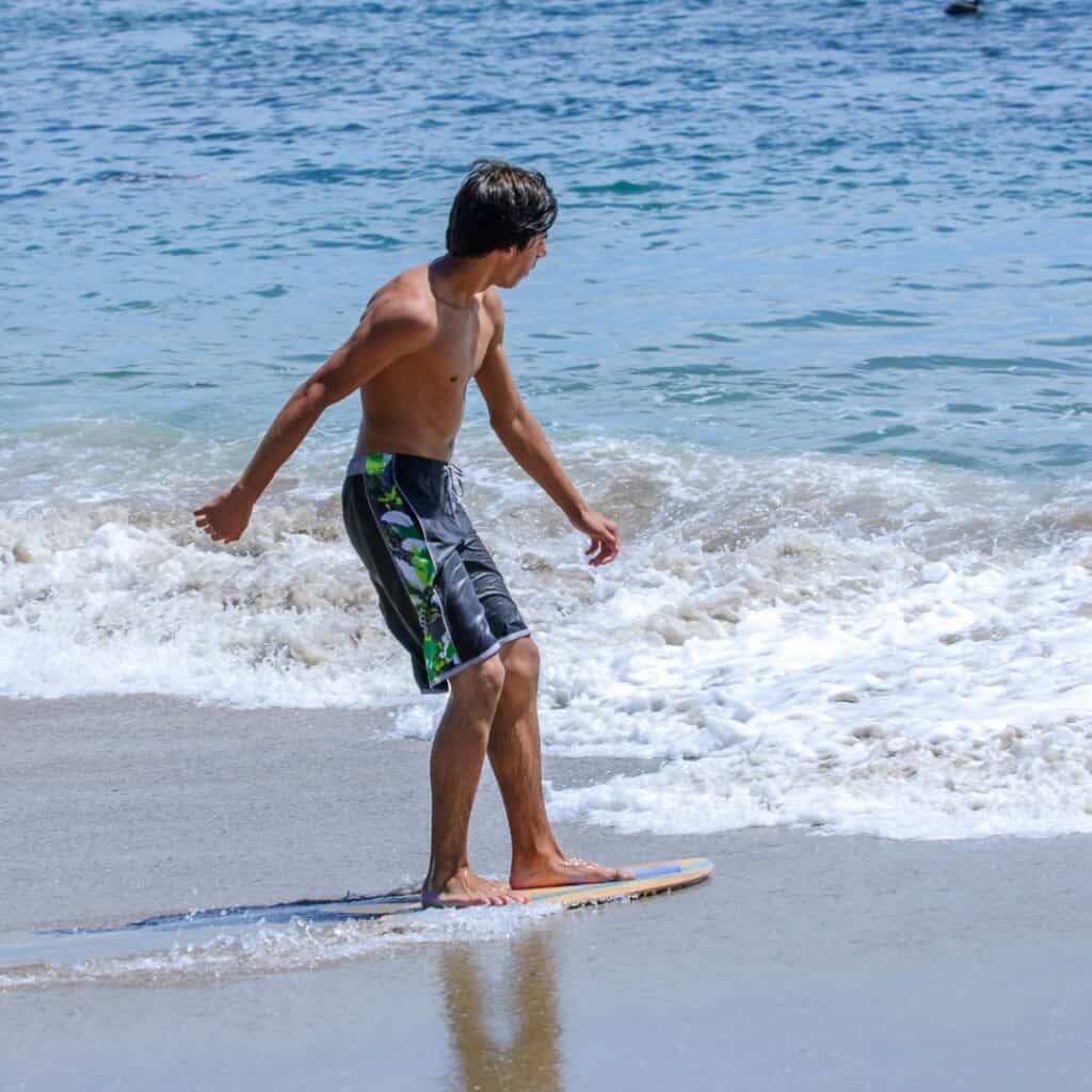 a person standing on a skimboard at the beach.